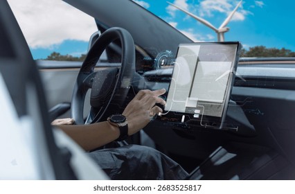 Close-up of driver interacting with advanced touchscreen dashboard inside a modern electric vehicle, with wind turbines visible outside the window.