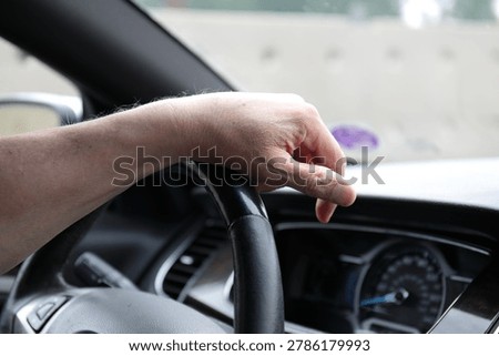Close-up of a driver s hand resting on the steering wheel, suggesting fatigue after a long drive. Concept of road travel, exhaustion, concentration, endurance, transportation, and the human side of driving.