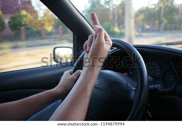 Close-up of driver\'s\
hands flipping the bird, giving the finger on 90ies, early 2000 car\
steering wheel. 