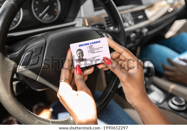 Closeup of driving license in unrecognizable\
black lady hands, african american woman driving school student\
celebrating successful graduation, sitting in car with instructor,\
cropped