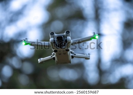 Close-up of a drone in flight, viewed from underneath at an angle, with green navigation lights and a blurred forest background.