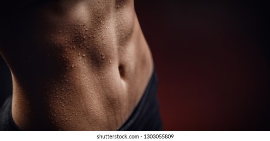 Closeup of drop of sweat on skin abdomen woman after workout. Dark background.