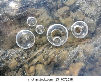 A Close-up Of Droplets Hanging From The Ice Surface On A Frozen Puddle, With Gravel Shining Through. All Gone 2 Hours Later. March, 24, 2019.