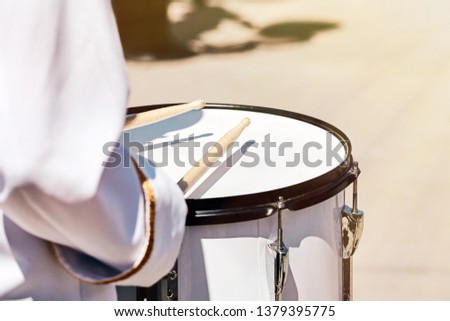 Closeup of a drummer's hand from an ensemble of drummers in a white formal dress, performing in the spring in a city park.