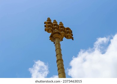 Close-up of the Dwajasthambam golden religious hanging bell pole in the temple against the blue sky.