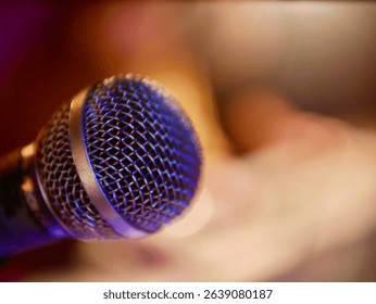 Close-up of a dynamic stage microphone under warm and colorful lighting. Abstract background with shallow depth of field. Music performance, concert, or podcast concept.