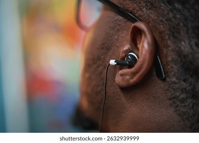 Close-up of ear with earphones plugged in listening to music. Background is blurred, drawing focus on ear and earphones
