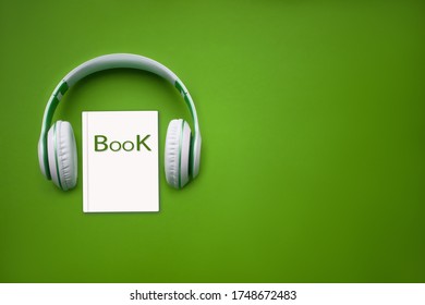 Close-up Earphones And Audiobook On Green Background. Audio, Listen. Audiobook Concept