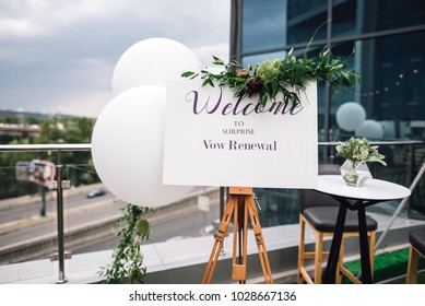 Closeup Of Easel With White Welcome Sign On Frame Stands On The Roof Top During Wedding Party. Vow Renewal