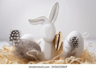 Close-up of Easter bunny holding golden carrot, eggs with delicate color pattern in straw nest. Easter decoration at home. Greeting card or invitation, copy space. Happy Easter holidays - Powered by Shutterstock