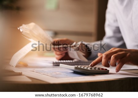 Close-up of economist using calculator while going through bills and taxes in the office. 