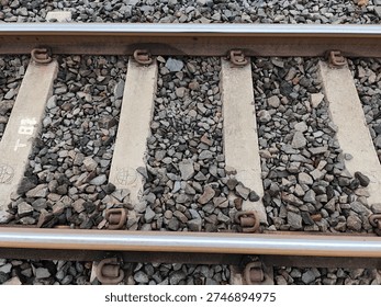 Close-up of elastic rail clips (e-clips) fastening a steel railway track to a concrete sleeper with stone ballast background. Detail of railway infrastructure and permanent way engineering