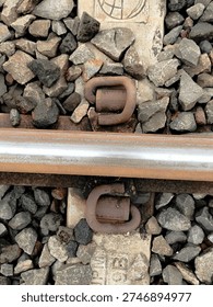 Close-up of elastic rail clips (e-clips) fastening a steel railway track to a concrete sleeper with stone ballast background. Detail of railway infrastructure and permanent way engineering
