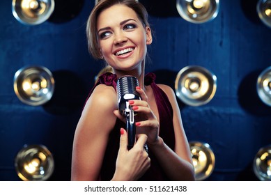 Close-up Of Elated Young Woman Singing In A Silver Vintage Microphone Wearing Vinous Evening Dress. Using Studio Microphone And Posing At The Camera