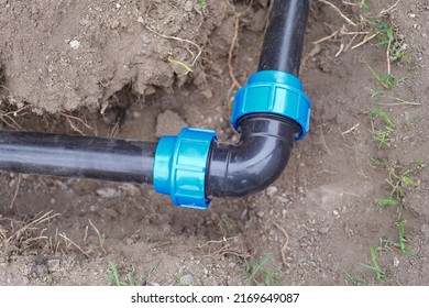 Close-up Of Elbow Fitting And Pvc Pipes At Bend In Dirt Trench Outdoors. Plumbing Water Drainage Installation. Underground Irrigation System Concept