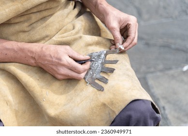 Close-up of an elderly blacksmith's hands resting on his brown leather apron polishing an iron work with his working tools. - Powered by Shutterstock