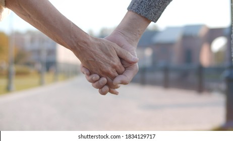 Close-up Of Elderly Couple Holding Hands Over Blurred House On Background