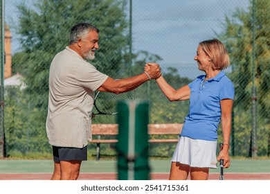 closeup elderly couple of tennis players shares warm handshake, smiling at each other before their match, with the net visible between them. reflects their camaraderie and enthusiasm for the game - Powered by Shutterstock