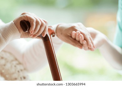 Closeup of elderly lady holding walking cane in one hand and holding volunteer's hand in the other - Powered by Shutterstock