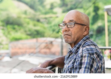 close-up of an elderly latin man with brown skin and glasses, standing with his hands on the railing of a balcony at home, observing nature and thinking about his long life. concept of retirement - Powered by Shutterstock