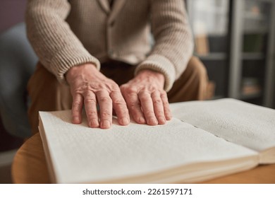 Close-up of elderly man sitting at table at home and reading a book in Braille using his hands - Powered by Shutterstock