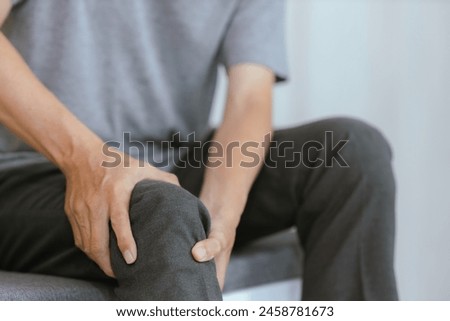 Close-up of an elderly man whose ankle hurts from walking too much. Massage painful feet and knees Calf pain sitting on the sofa at home