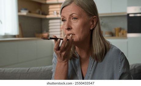 Close-up elderly mature Caucasian woman female grandmother talking on phone using speakerphone at home command internet assistance recording voice message on smartphone mobile ai technology concept - Powered by Shutterstock