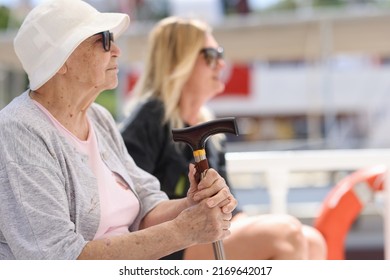 Close-up Of Elderly Woman With Cane Sitting On Bench. Tired Grandmother Resting Outside Or Waiting Public Transport. Old Age Concept