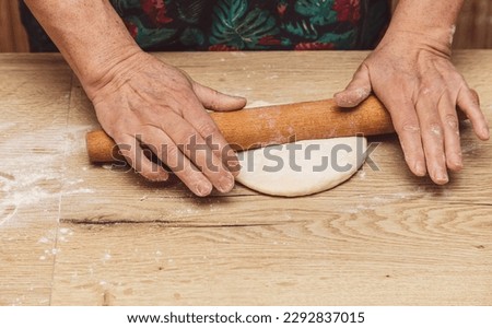 Close-up of an elderly woman rolling dough with a rolling pin.