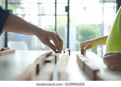 Close-up of elderly woman and young boy hands playing with wooden blocks on a table, focusing on intergenerational bonding activity - Powered by Shutterstock