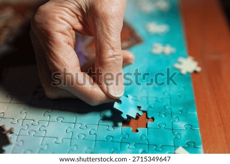 closeup of elderly woman's hand while she assembles jigsaw puzzle on wooden table