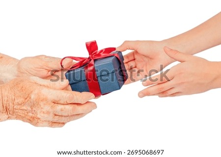 Close-up of elderly and young hands exchanging a blue gift box with a red ribbon, isolated on white. Symbolic concept of giving, care, gratitude, connection, family love between generations.