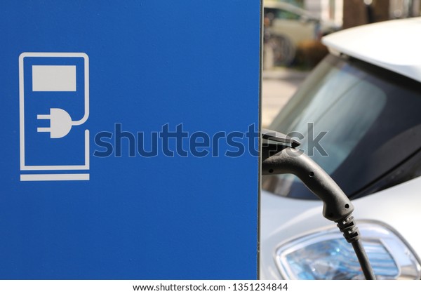 Closeup of electric cars charging station with plug-in\
charger plugged into rechargeable batteries motor of parked\
vehicles. Concept of green clean environment, reduction of\
emissions, air pollution\
