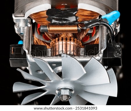 Closeup of electric DC motor inside and fan metal vanes on steel shaft. Rotor copper commutator and stator wire winding, carbon brushes and choke or capacitor in electrical engine on black background.