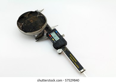 Closeup Of An Electric Digital Caliper Being Used To Measure The Outer Diameter Of A Damaged Motorcycle Piston Against A Light, Neutral Background.