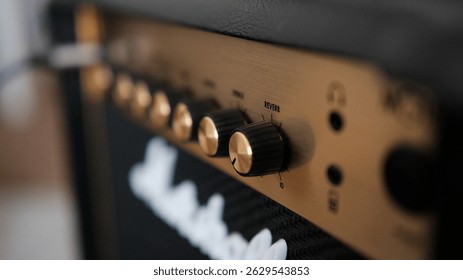 Close-up of electric guitar amplifier knobs with shallow depth of field, isolated from background. The textured surface and detailed controls evoke a sense of analog warmth and musical craftsmanship. 