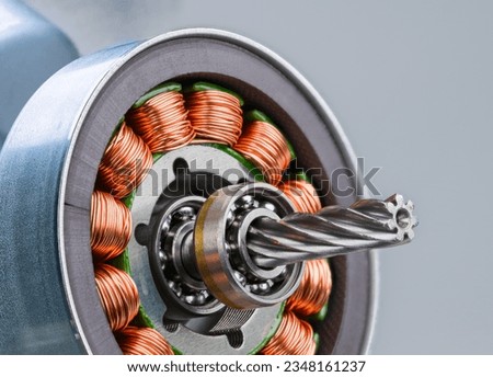 Closeup of electric motor rotor with worm gear, ball bearing and inductors on gray background. Copper wire winding on electromagnetic coils with metal sheets inside steel bushing of electrical engine.