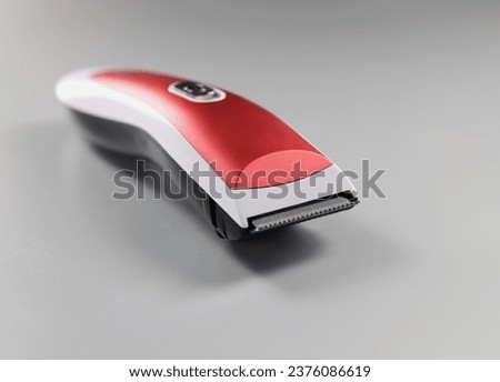 Close-up of electric trimming machine for hair, device with red colour design on grey surface. Equipment to create hairstyle. Hairdresser, barber concept