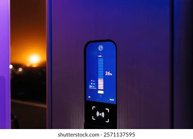 A close-up of an electric vehicle charging station screen showing a 26 percent battery level and real-time charging statistics under vibrant neon lights.