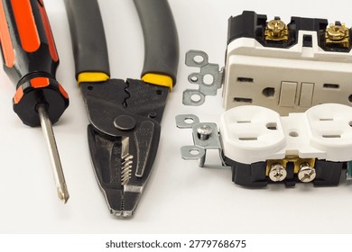 Close-up of electrical outlets, screwdriver, and wire stripper tools on a white background, illustrating electrical installation, home wiring, maintenance, repair work, and DIY projects.