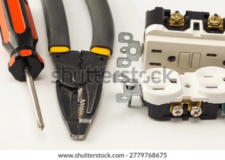 Close-up of electrical outlets, screwdriver, and wire stripper tools on a white background, illustrating electrical installation, home wiring, maintenance, repair work, and DIY projects.