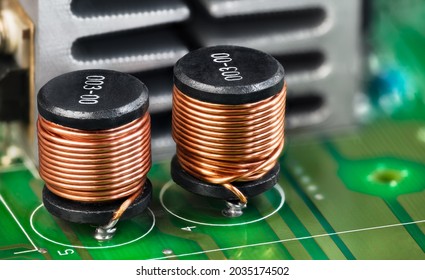 Closeup of electronic coils and metal cooler on green printed circuit board detail. Ferromagnetic inductors with copper wire winding or aluminum heat sink on PCB. Components in electrical engineering.