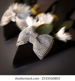 Close-up of elegant black high heels adorned with sparkling rhinestone bows and white flowers in soft focus background. - Powered by Shutterstock