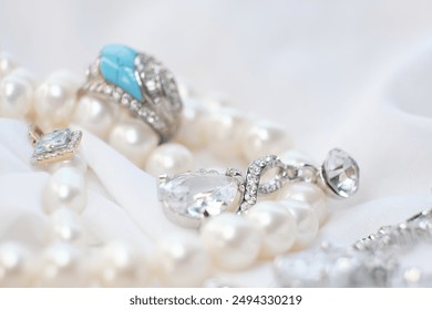 Close-up of elegant jewelry pieces, including pearls, silver rings, and a blue gemstone ring on a white fabric background. This image captures the luxury and sophistication of fine jewelry