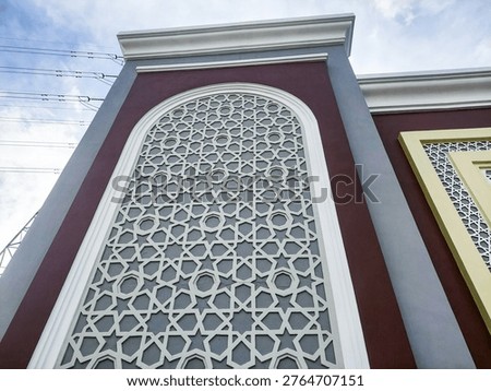 Close-up of elegant mosque wall texture featuring Islamic geometric pattern lattice, arched design, and modern architectural details against a blue sky.