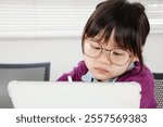 Close-up of an elementary school girl with glasses operating a tablet and studying.