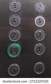 Close-up of an elevator control panel with numbered floor buttons and Braille markings. The zero button is illuminated, indicating floor selection.