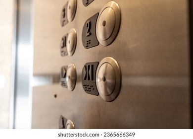 A close-up of an elevator control panel - stainless steel with round buttons - numbers and braille - emergency call and door open buttons