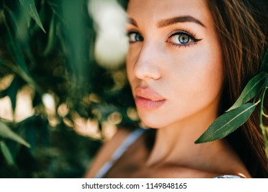 Closeup emotional artistic portrait of amazing fabulous beautiful young cheerful model girl with big natural lips and blue passionate eyes looking at camera outdoor at nature.  Cute lovely teen face