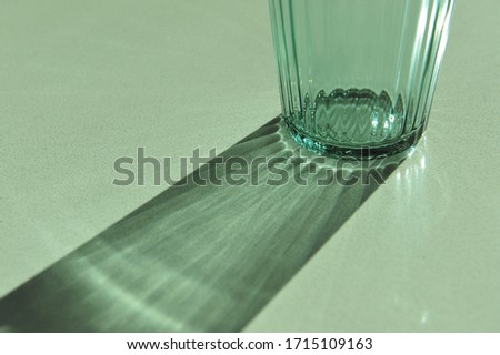Closeup of empty green texture fluted glass disperse strong beam of sunlight into mixture of stripe shadow and reflection on synthetic stone table top. Mixture of shadow and reflection stripe 